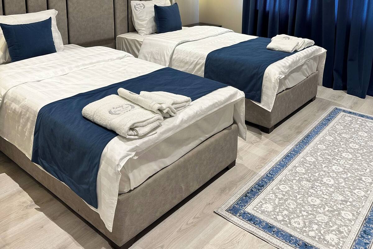 A hotel room with two beds, a large painting, a wall-mounted light, and a blue curtain.