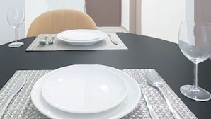 A dining area with a round table set for two, including plates, cutlery, and a wine glass. - Urban Charm: Studio With Balcony in Azizi Riviera (Dubai)