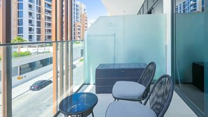 A balcony with a view of a cityscape, a black chair, and a small table. - Urban Charm: Studio With Balcony in Azizi Riviera (Dubai)