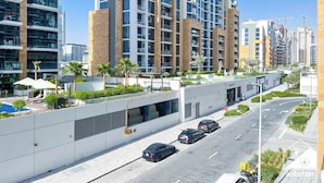 A modern apartment building with multiple floors, balconies, and a rooftop garden. - Urban Charm: Studio With Balcony in Azizi Riviera (Dubai)