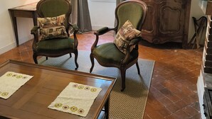 A living room with two green upholstered chairs, a wooden coffee table, a television, and a large window with curtains. - Maison Play (Roumoules)