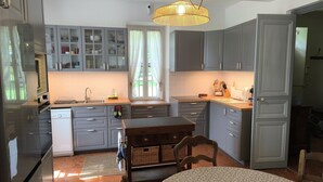 A compact kitchen with grey cabinets, a built-in oven, a sink, and a dining area with a table and chairs. - Maison Play (Roumoules)