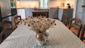 A dining table with a floral tablecloth, surrounded by wooden chairs, in a kitchen with grey cabinets and a window. - Maison Play (Roumoules)