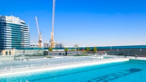 A swimming pool with a view of a construction site and a modern building. - Stylish 1BR With Balcony City Views O2 Tower, JVC (Dubai)