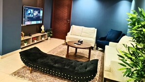 Una sala de estar moderna con un televisor de pantalla plana, un sofá negro, un sofá blanco, un sofá azul, una mesa de centro y una planta en maceta.