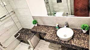 Un baño moderno con encimera de granito, un lavamanos blanco y dos plantas en macetas.