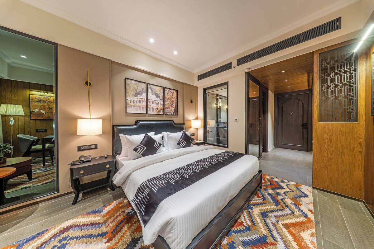 Une chambre d’hôtel moderne, dotée d’un grand lit, d’une table de chevet, d’un miroir et donnant sur le couloir.