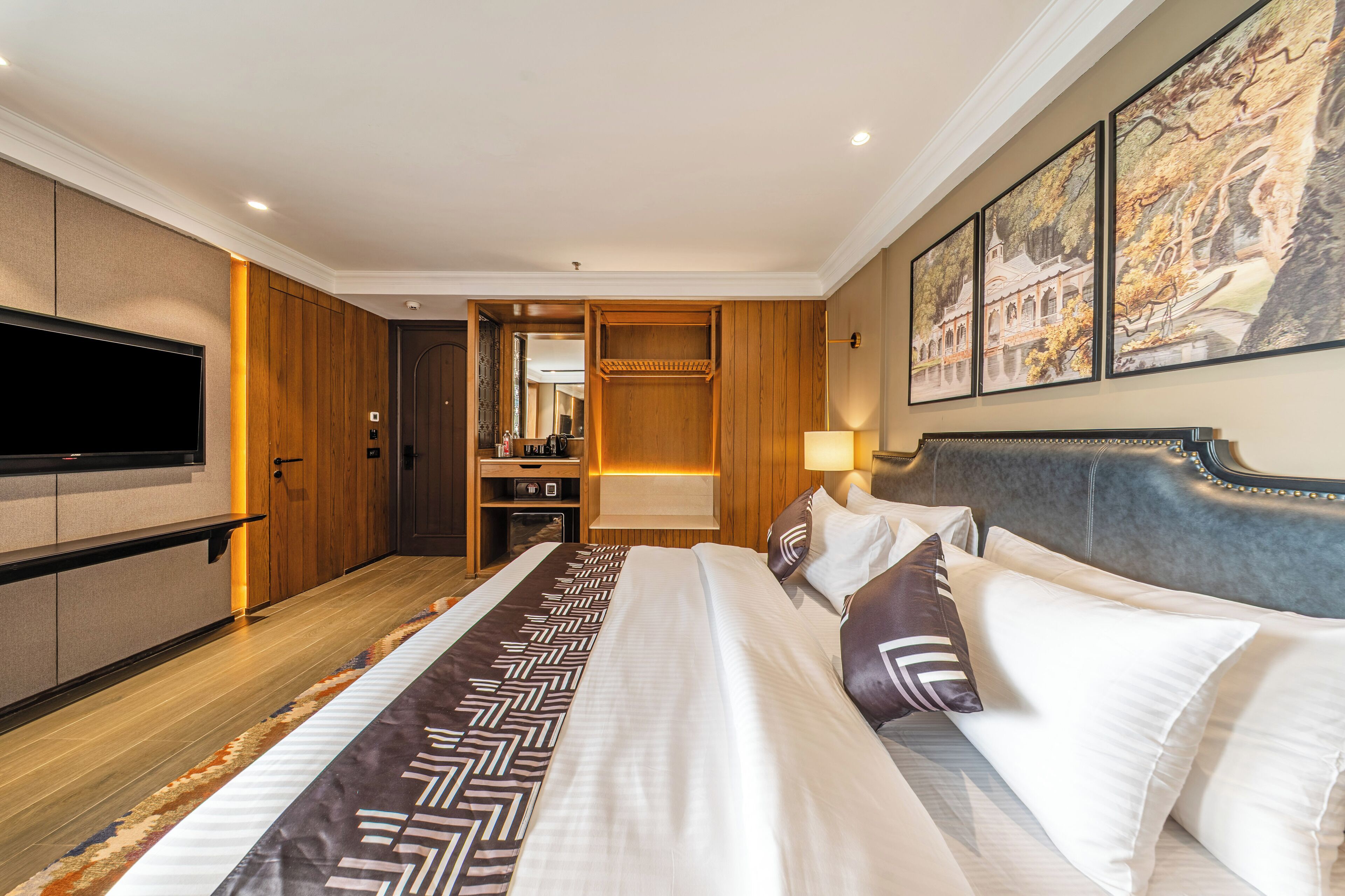 A hotel room with a large bed, a flat-screen TV, wooden paneling, a walk-in closet, and a painting on the wall.