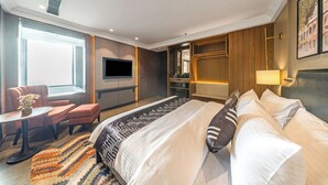 Ein modernes Hotelzimmer mit einem großen Bett, einem Fernseher, einem Schreibtisch und einer Sitzecke.
