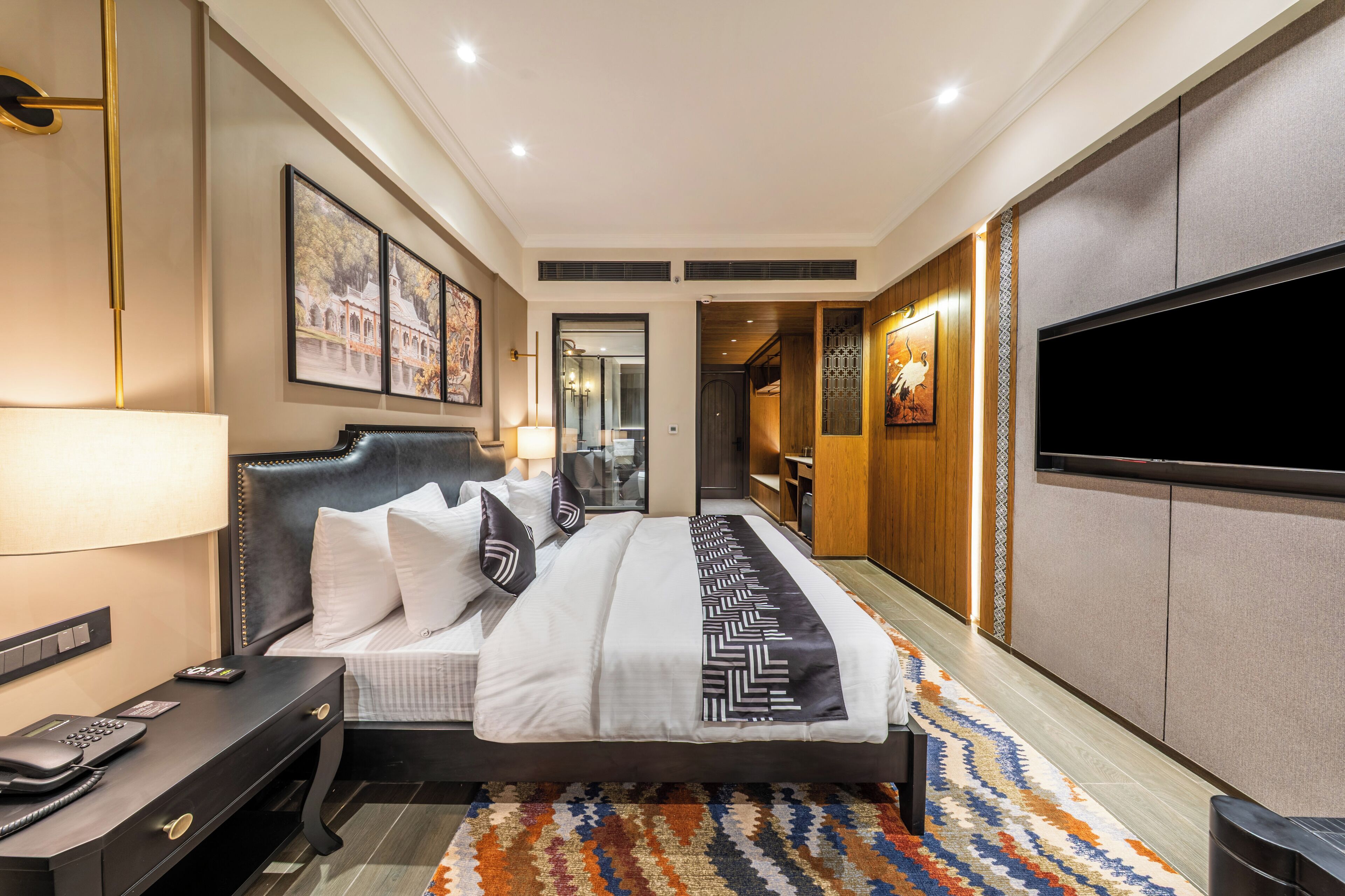 Camera d'albergo moderna con un letto grande, una scrivania con il telefono, una TV a schermo piatto fissata al muro e un tappeto decorato.