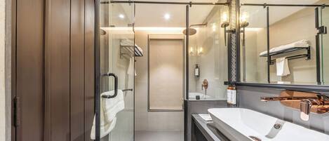 Ein modernes Badezimmer mit einer Glastrennwand-Dusche, einem großen weißen Waschbecken und einem Spiegel mit schwarzem Rahmen.