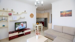 A modern living room with a flat-screen TV, a dining table with chairs, a sofa, and a kitchen in the background. - Seascape Sea view Apartment (Vlorë)