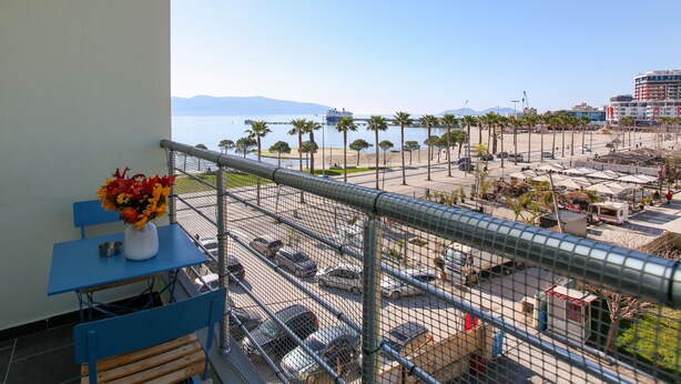 A balcony with a table and chairs, overlooking a parking area and a beach with palm trees. - Seascape Sea view Apartment (Vlorë)