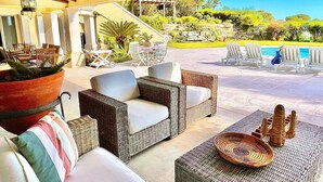 An outdoor seating area with wicker furniture, a large planter, and a view of a pool and greenery.