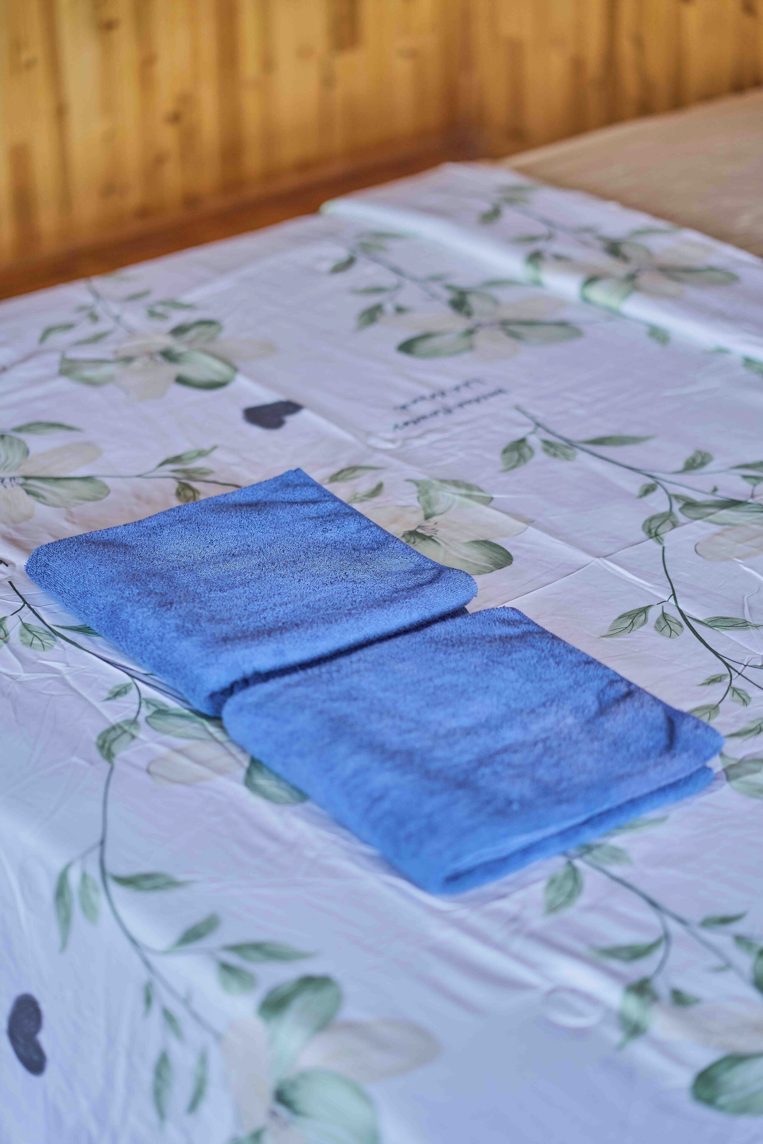 Una cama con una colcha estampada con motivos florales y dos toallas azules dobladas.