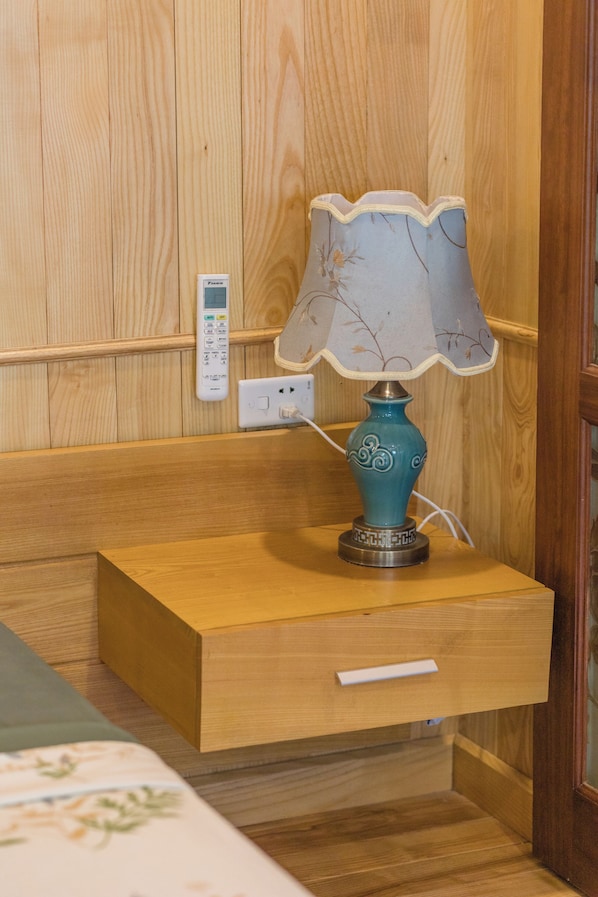 A wooden bedside table with a teal lamp, a power outlet, and a thermostat on the wall. - Lan Ha Floating Homestay (Hai Phong)