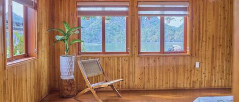 A wooden-paneled room with large windows, a potted plant, a chair, and a bed.