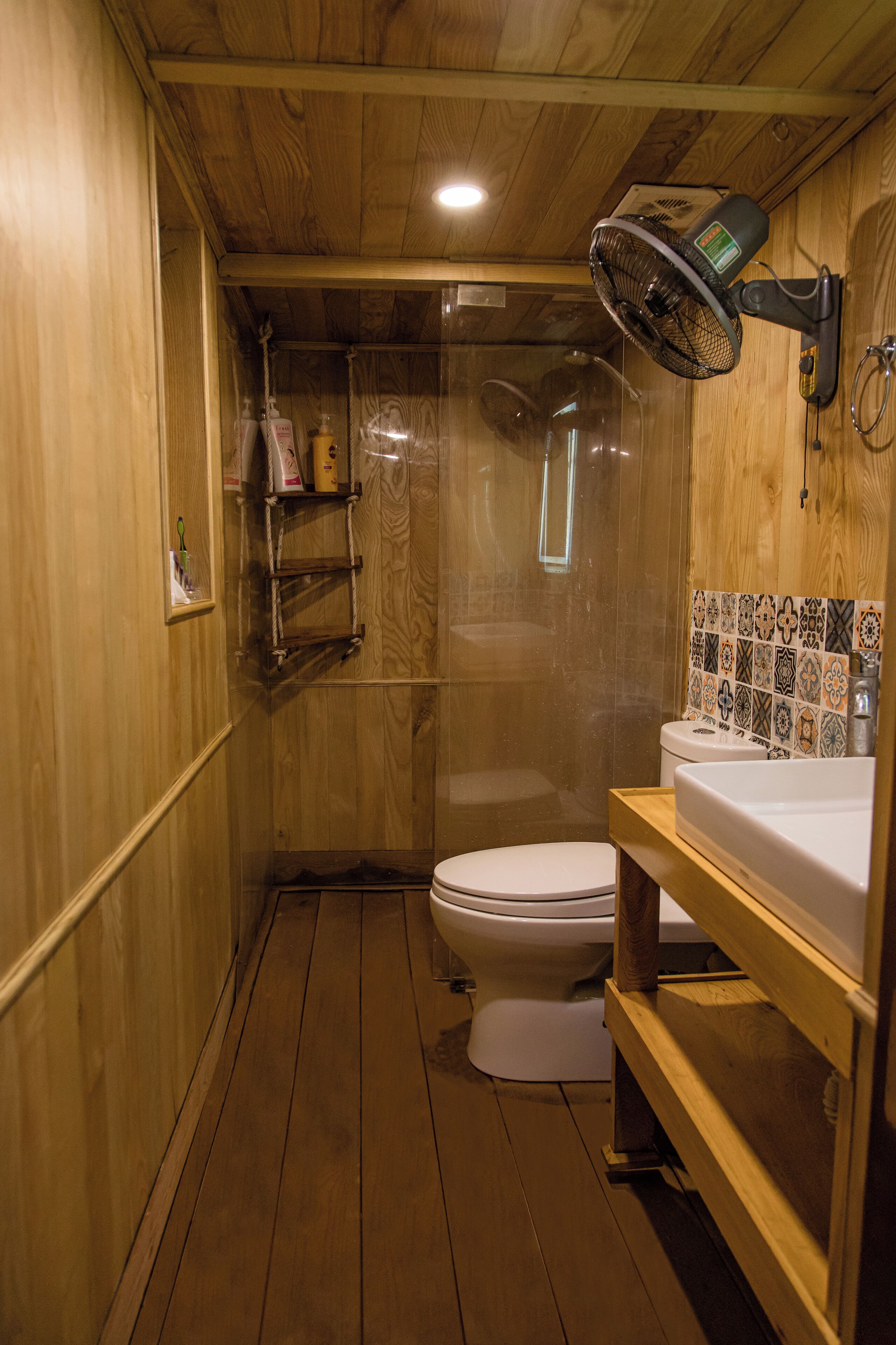 A wooden-floored bathroom with a toilet, a shower enclosure, and a sink with a tiled backsplash.