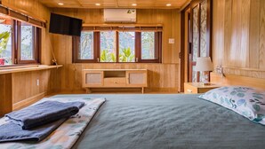 Une pièce en bois avec un lit, une télévision, un bureau et des fenêtres ornées de plantes.