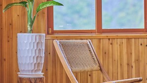 A wooden room with a large window, a potted plant, and a wicker chair. - Lan Ha Floating Homestay (Hai Phong)