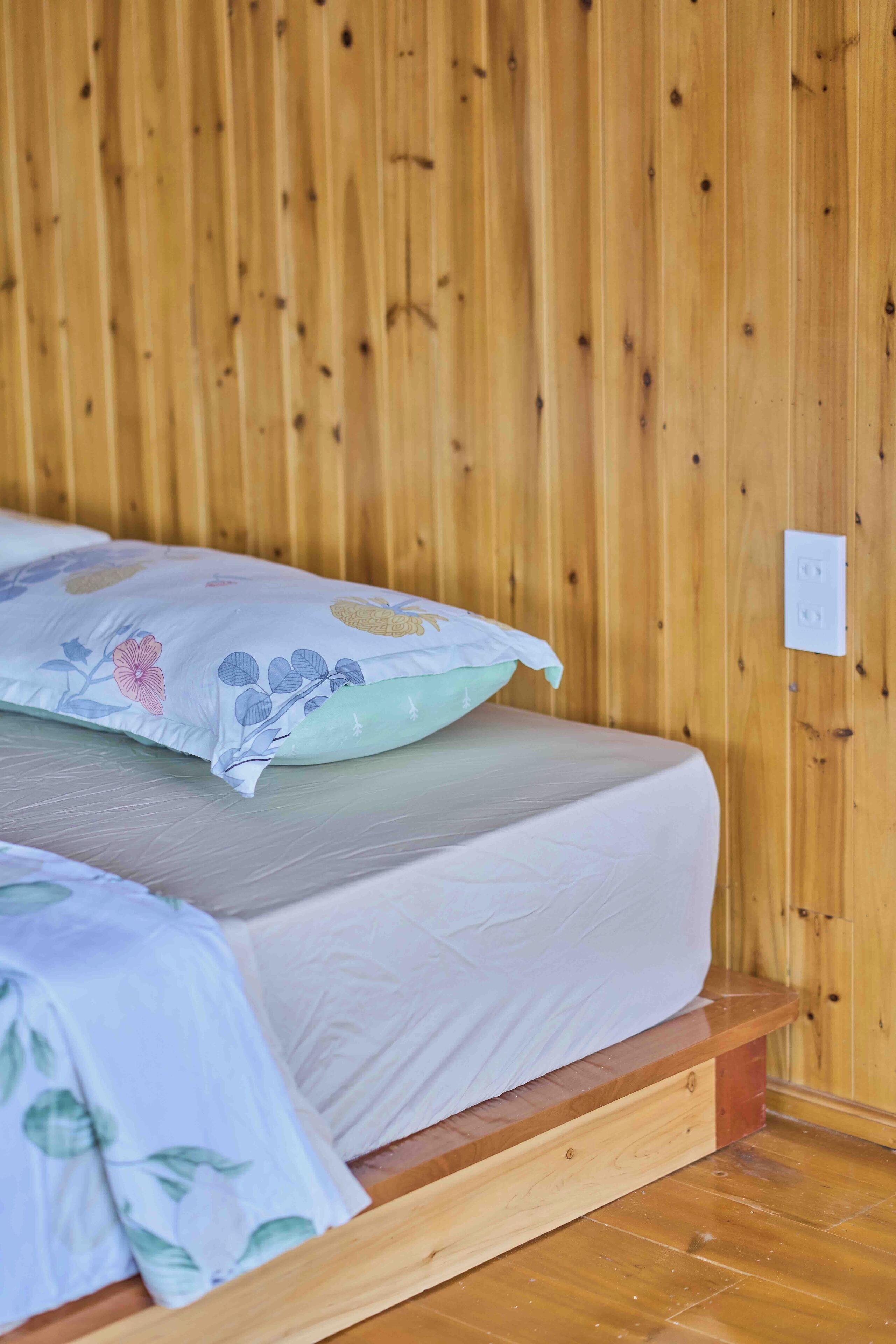 A wooden bed with a white mattress and floral-patterned pillows.