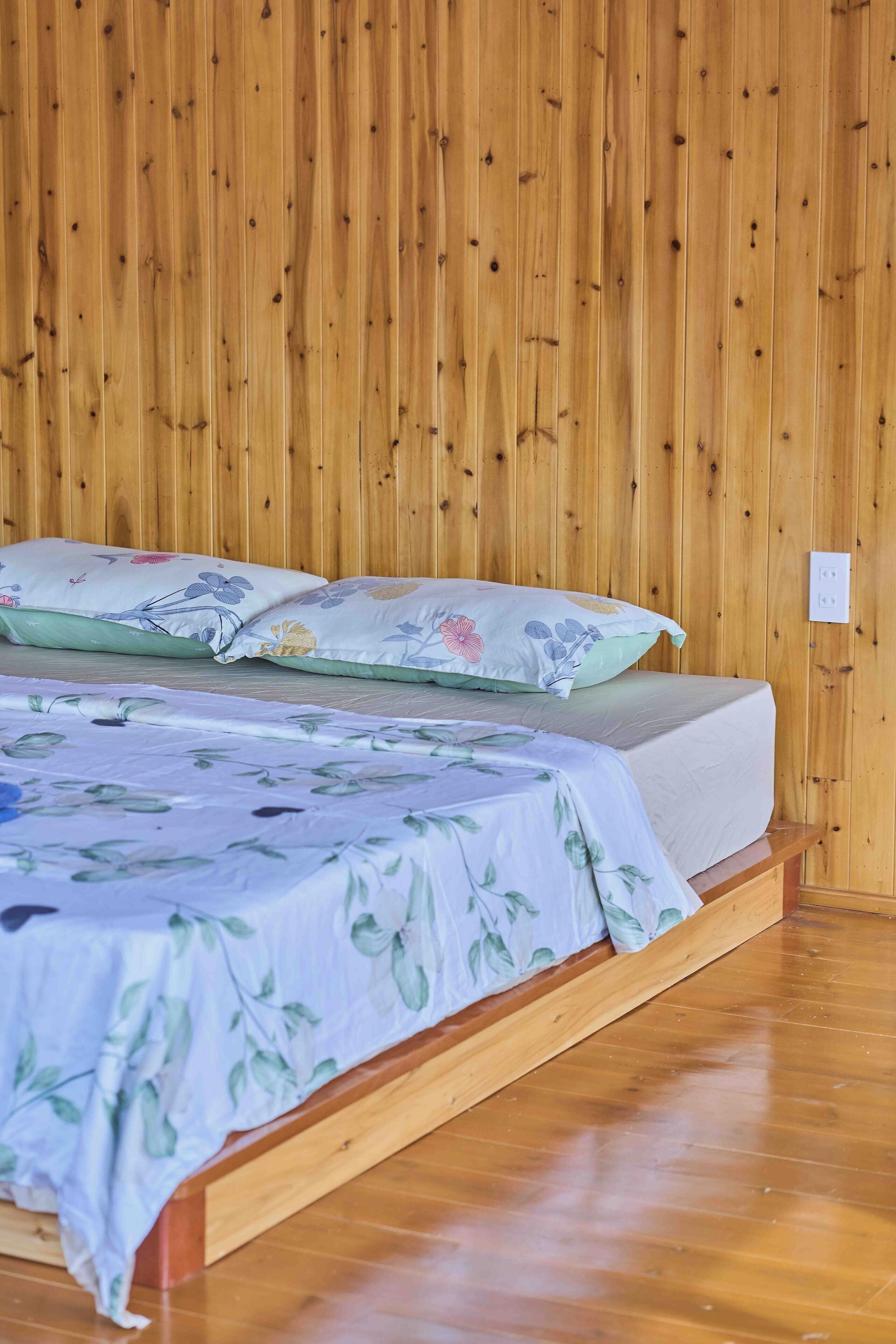 Ein Zimmer mit Holzwänden, einem Bett mit floralem Bettzeug und einem hölzernen Gestell.