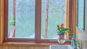 A wooden cabin bathroom with a window overlooking a lake, a sink, and a ladder. - Lan Ha Floating Homestay (Hai Phong)
