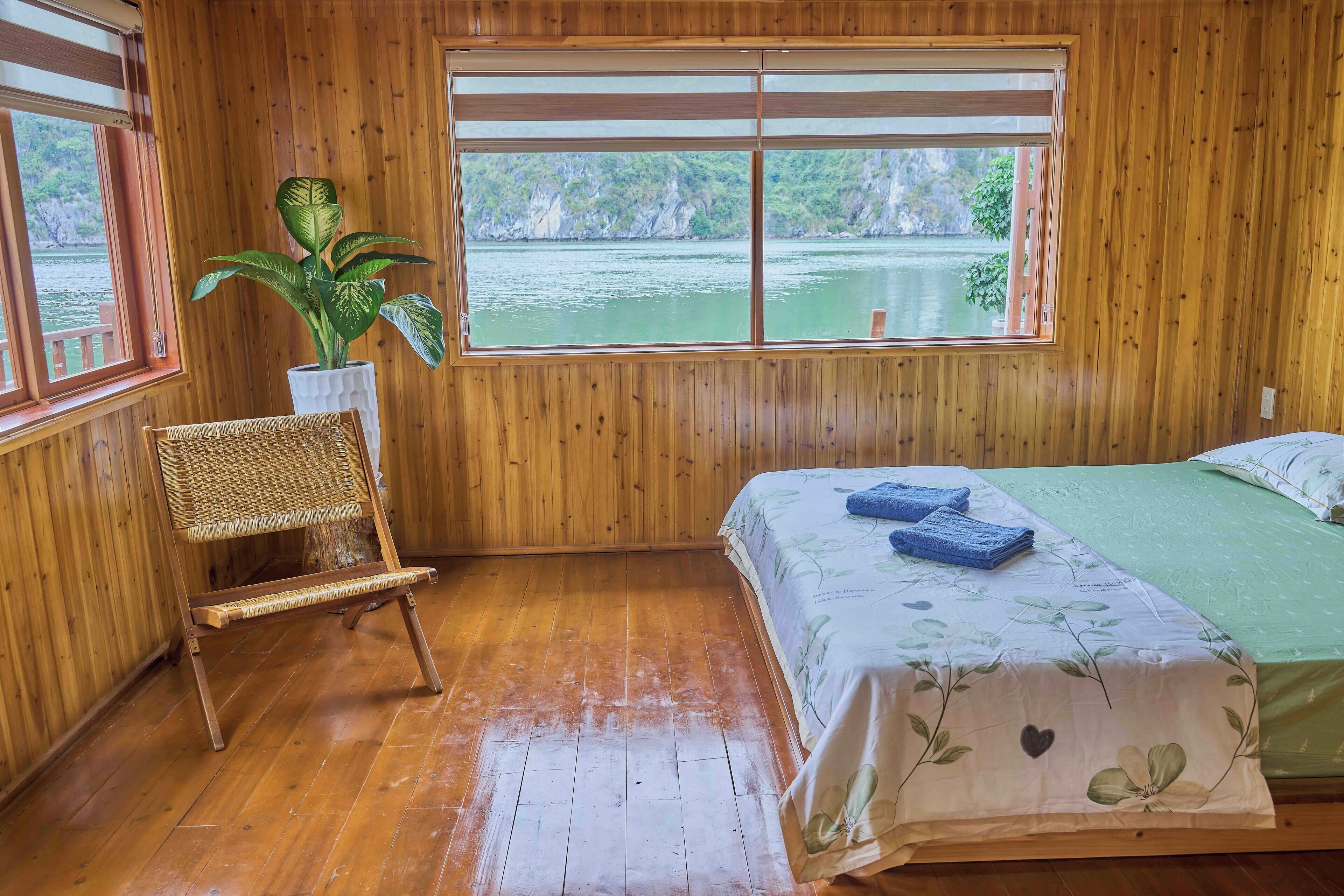 A wooden room with a bed, a chair, a window, and a plant.