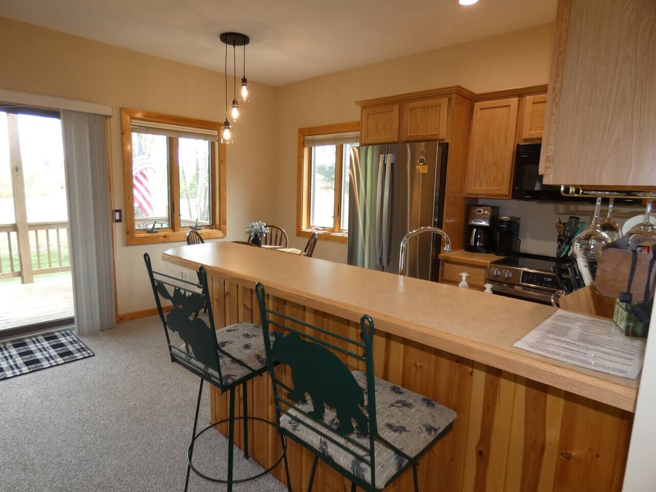 A kitchen with wooden cabinets, a stainless steel refrigerator, a coffee maker, and a bar with stools.