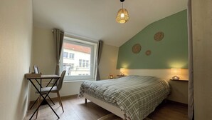 Une chambre à coucher comprenant un lit, un bureau, une chaise, une fenêtre avec des rideaux, un luminaire suspendu et un mur décoré d’assiettes.