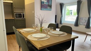 Un coin repas avec une table en bois, dressée pour quatre personnes et entourée de chaises, dans une cuisine moderne équipée d’un four à micro-ondes et de placards.