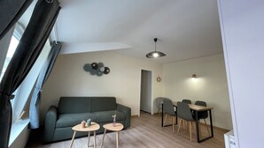 Un salon moderne comprenant un canapé, deux petites tables, une table à manger avec des chaises et un luminaire au plafond.