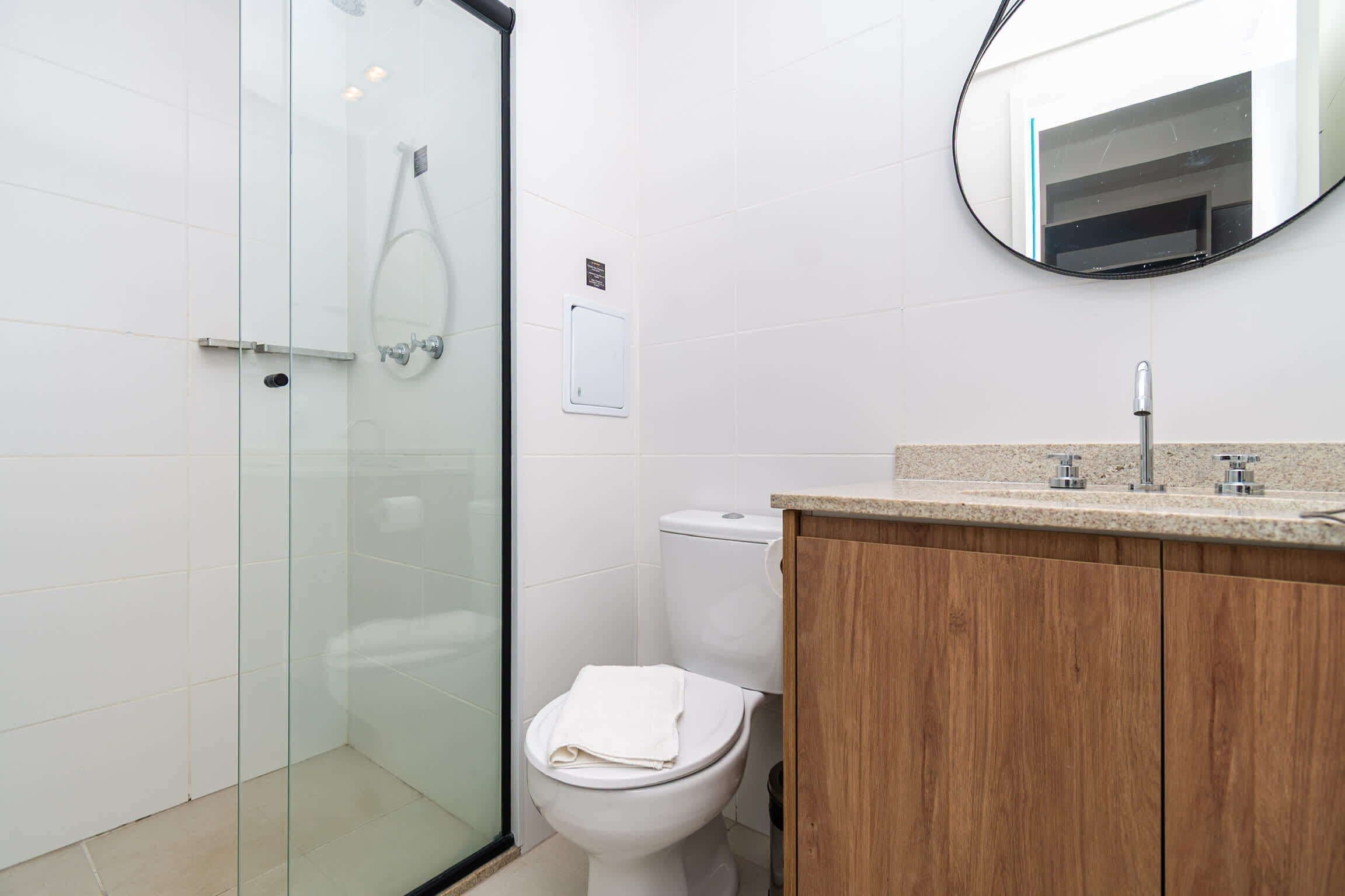 Een moderne badkamer met een glazen douchecabine, een wit toilet en een houten wastafelmeubel met een wastafel.