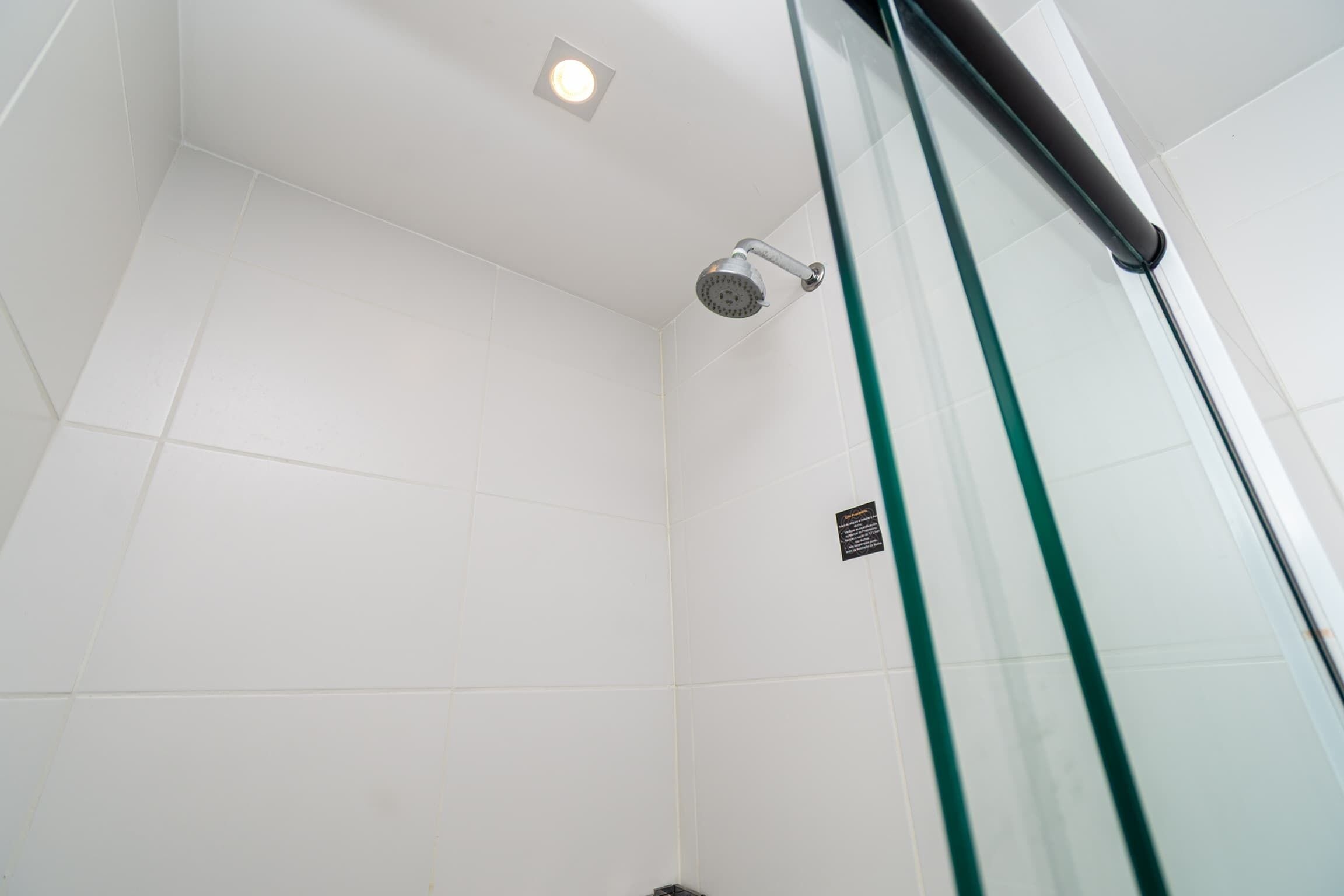 A shower with a glass door, white tiled walls, and a ceiling light.