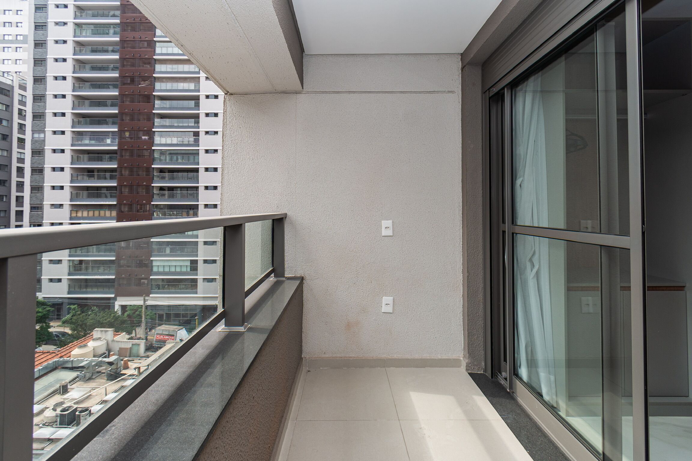 Un balcón estrecho con barandilla metálica, puerta de cristal y pared lisa.