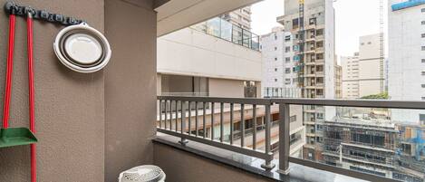 A balcony with a view of surrounding buildings, a wall-mounted air conditioning unit, and a broom leaning against the wall.
