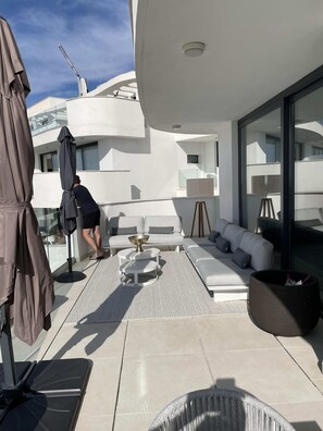 A modern outdoor living area with a sofa, a round table, and a large umbrella. - Huswell - Oceanview Stay in Higuer n West (Fuengirola)