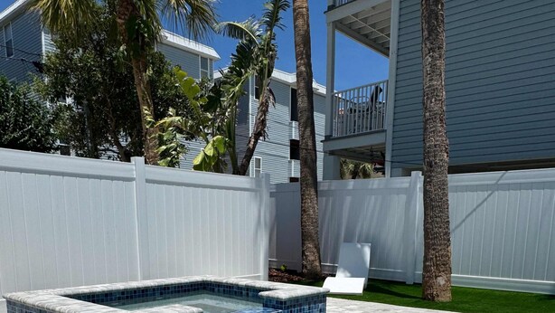 A swimming pool with clear blue water, surrounded by a white fence and palm trees. - Beach House Cottage Pool Spa on Beach Access (Indian Rocks Beach)