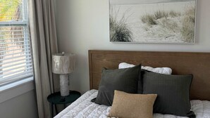 A bedroom with a bed, a nightstand, a lamp, and a painting on the wall. - Beach House Cottage Pool Spa on Beach Access (Indian Rocks Beach)