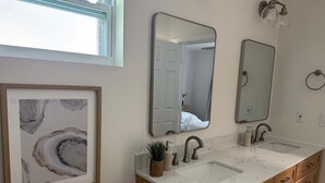 A bathroom with a double sink vanity, wooden cabinets, a framed abstract painting, and two wall-mounted mirrors. - Beach House Cottage Pool Spa on Beach Access (Indian Rocks Beach)