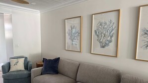 A living room with a grey sofa, a blue armchair, and two framed artworks on the wall. - Beach House Cottage Pool Spa on Beach Access (Indian Rocks Beach)