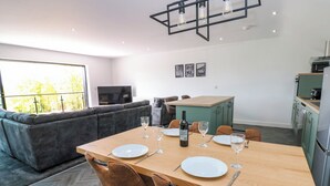 A modern living space with a dining area, sofa, kitchen, and a TV. - Sycamore Cottage (Frizington)