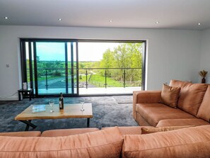 Un salon spacieux doté d’une grande fenêtre donnant sur une rivière et la verdure environnante.