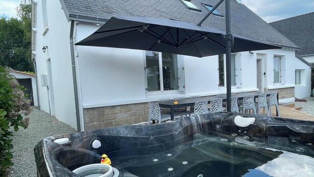 A hot tub with a black umbrella, surrounded by outdoor seating and a white house in the background. - New, seaside house, Beg meil, for groups and families  (Fouesnant)