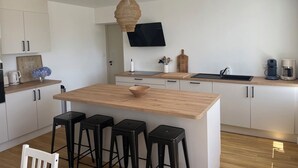 A modern kitchen with a central island, black stools, a wooden countertop, and a hanging light fixture. - New, seaside house, Beg meil, for groups and families  (Fouesnant)