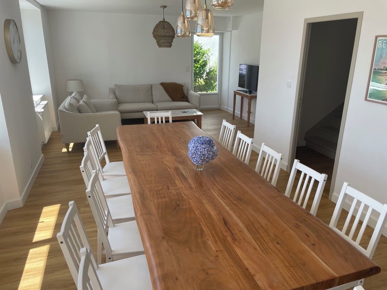 Een eetgedeelte met een houten tafel, omringd door witte stoelen, een bank en een televisie op de achtergrond.