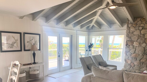 A spacious living room with a high ceiling, a stone accent wall, and a view of the ocean through large windows. - 3+ BR Beach ViewHouse (Palm Coast)