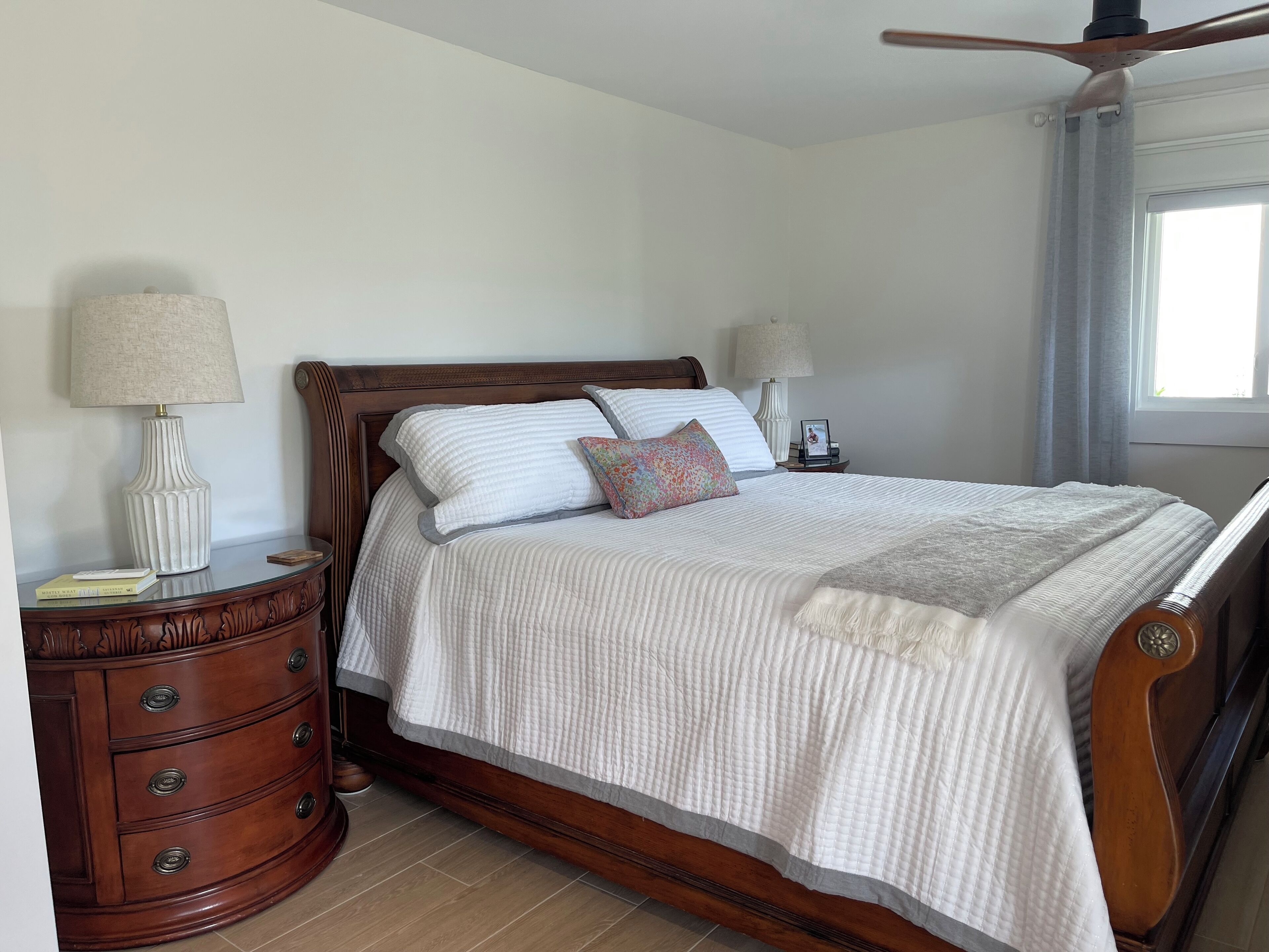 Een net opgemaakt bed met een houten hoofdbord, een nachtkastje met een lamp, en een ander nachtkastje met een lamp.