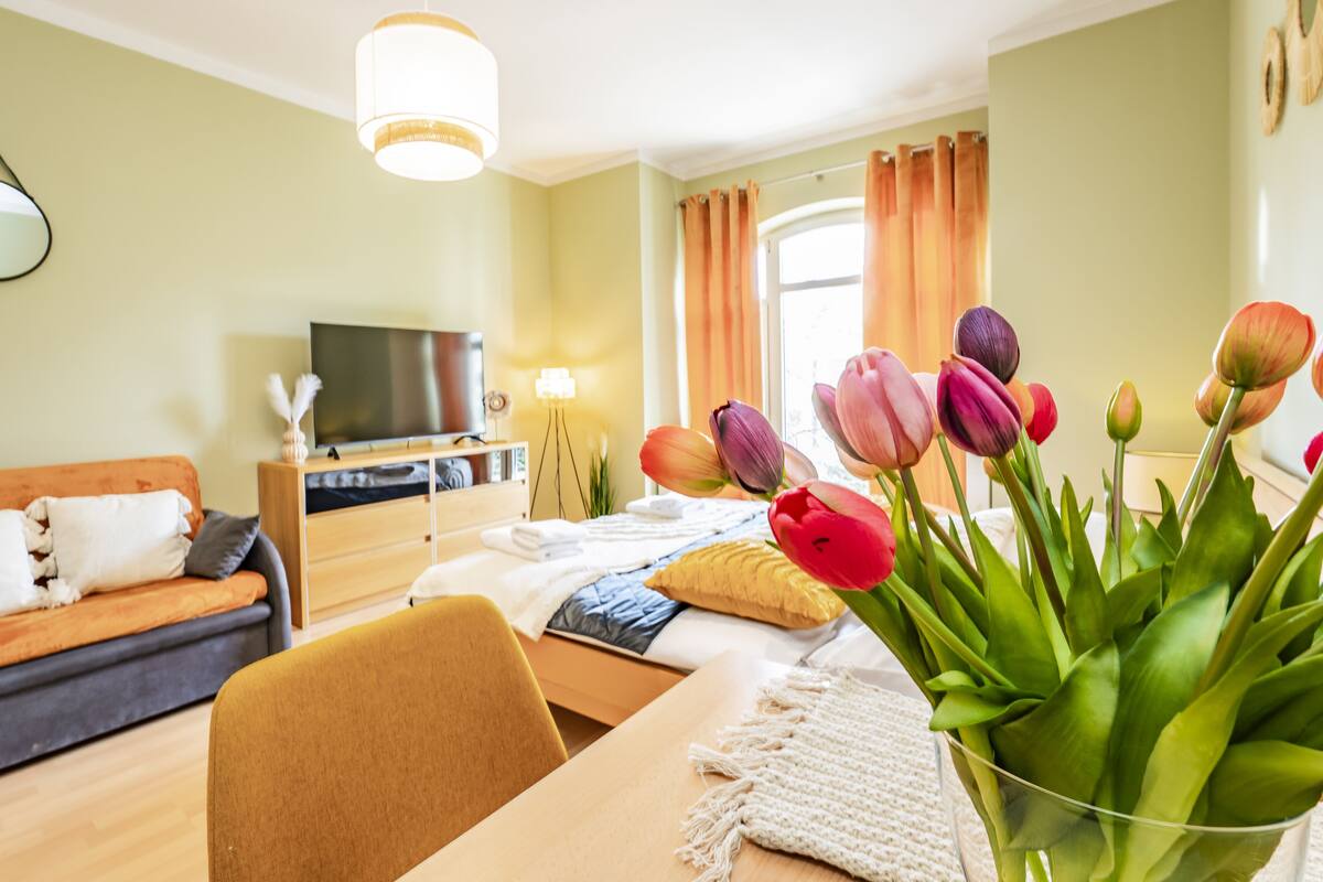 Habitación de hotel moderna con una cama, un sofá, un televisor, un escritorio y un jarrón con tulipanes.