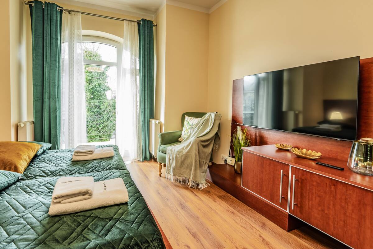 Una habitación de hotel con una cama, una silla verde, un armario de madera y un televisor.